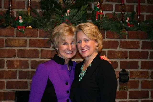 Two women standing together at a holiday gathering, reflecting women-led community impact.