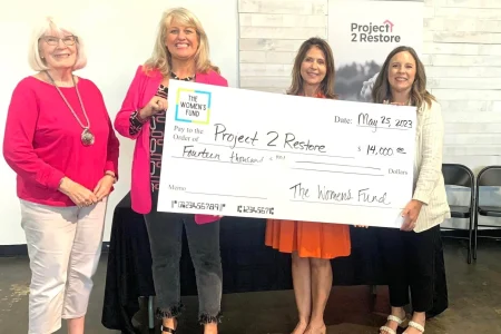 Four women presenting a $14,000 grant check to Project 2 Restore, emphasizing grants for women in Topeka.